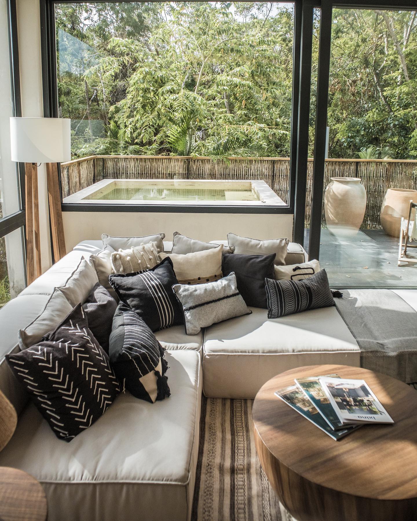 Sala moderna con sofá cama, cojines decorativos, lámpara y tapete texturizado.