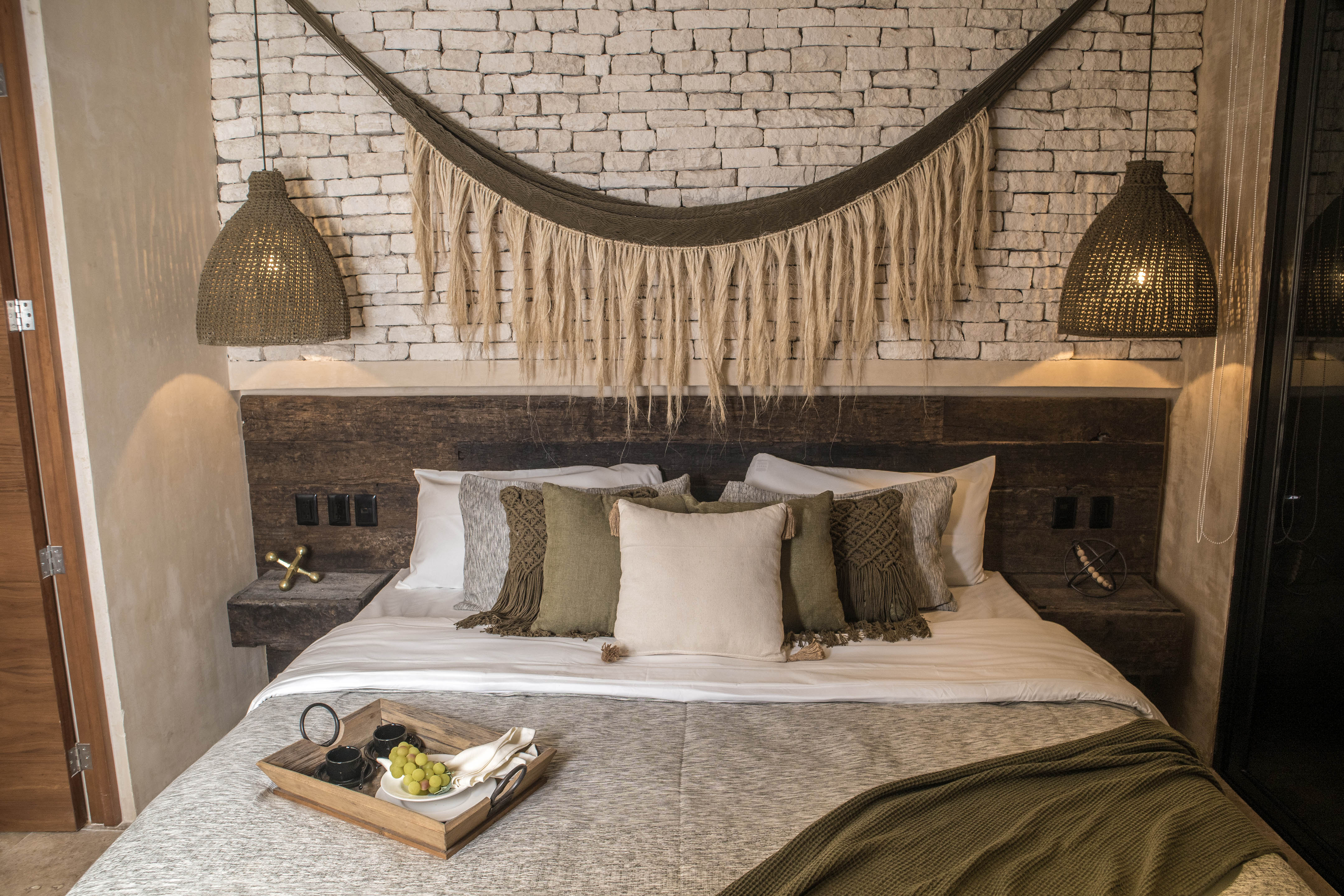 Recámara matrimonial decorada con textiles cálidos y cabecera rústica, ideal para renta vacacional en el Caribe.