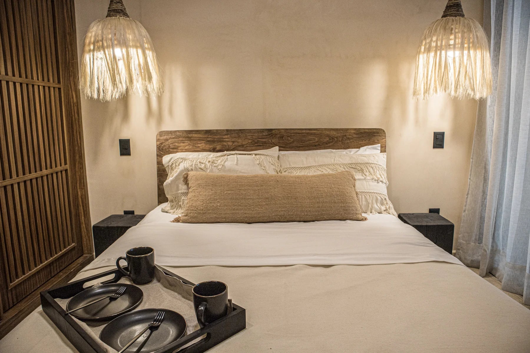 Recámara queen size con cabecera de madera, lámparas de techo colgantes y ambientación cálida para espacios de renta vacacional en Cancún, Playa del Carmen y Tulum.