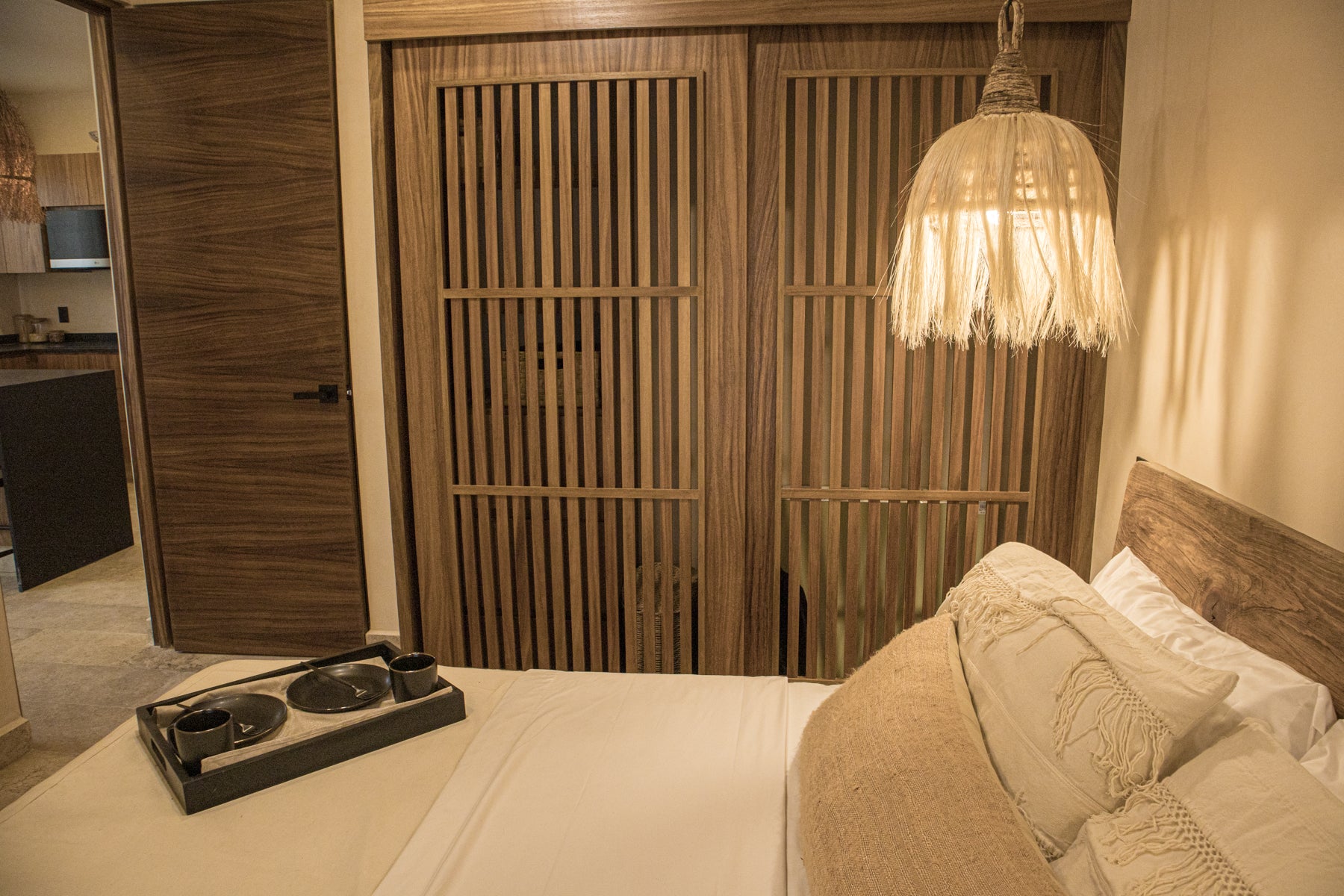 Habitación decorada con cabecera de madera, lámpara tejida y puertas corredizas de madera estilo moderno. Encuentra muebles para recámaras en Prisma Muebles Tulum.