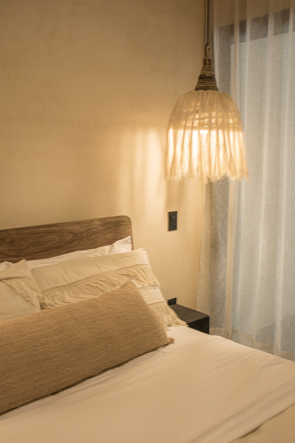 Habitación con cabecera de madera, lámpara colgante de fibras naturales y decoración costera. Disponible en Prisma Muebles, mueblería en Tulum.
