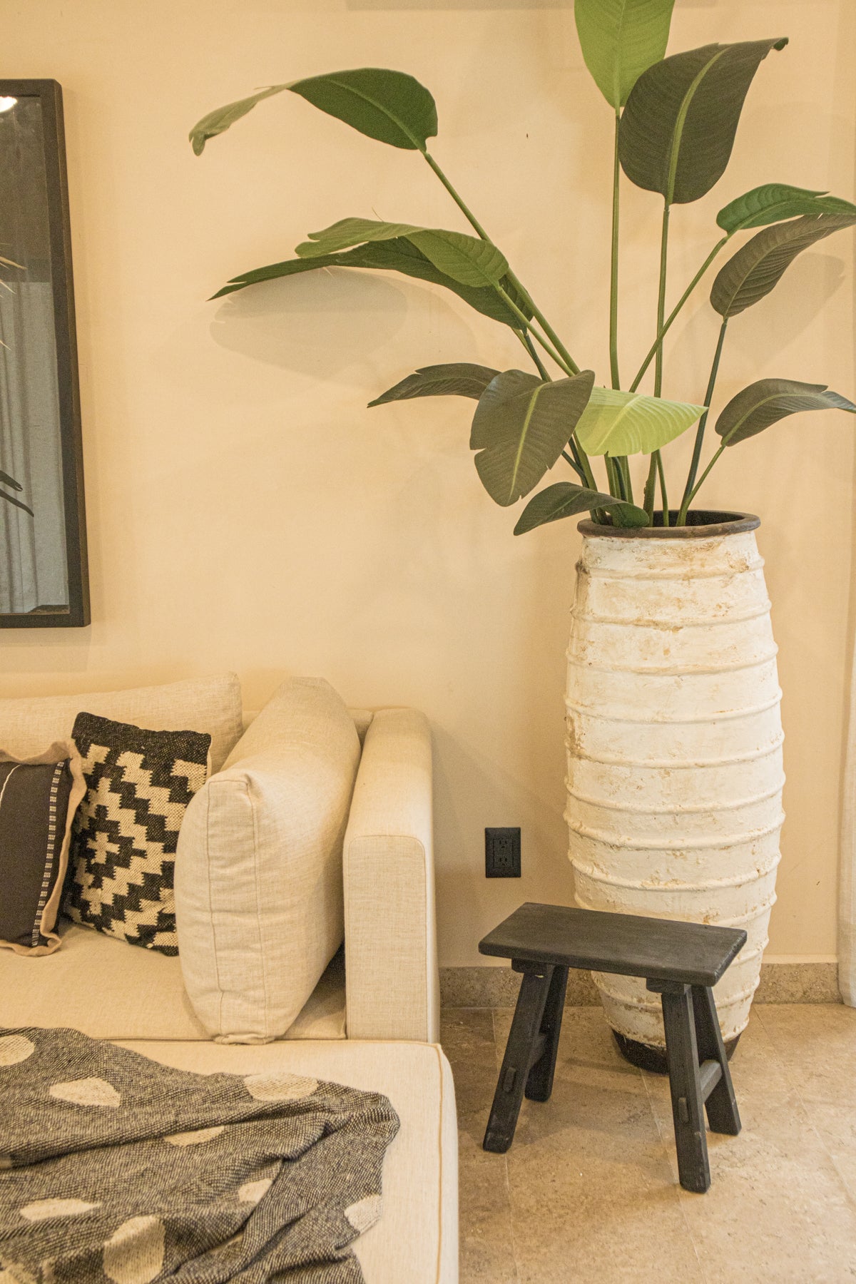 Sala en L en tono neutro, cojines con patrones geométricos y mesa lateral de madera junto a una maceta grande con planta tropical. Encuentra muebles y decoración costera en Prisma Muebles Tulum.