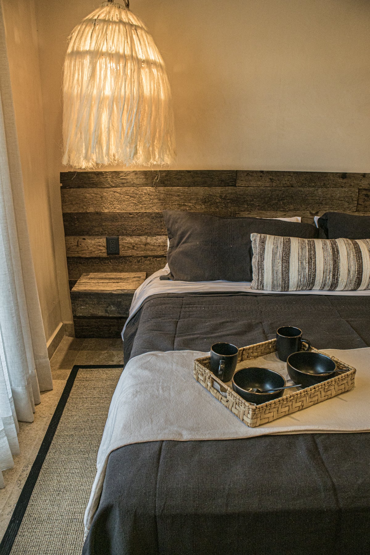 vista frontal de cama king size de madera con cojines decorativos, lámparas de techo tejidas con fibras naturales