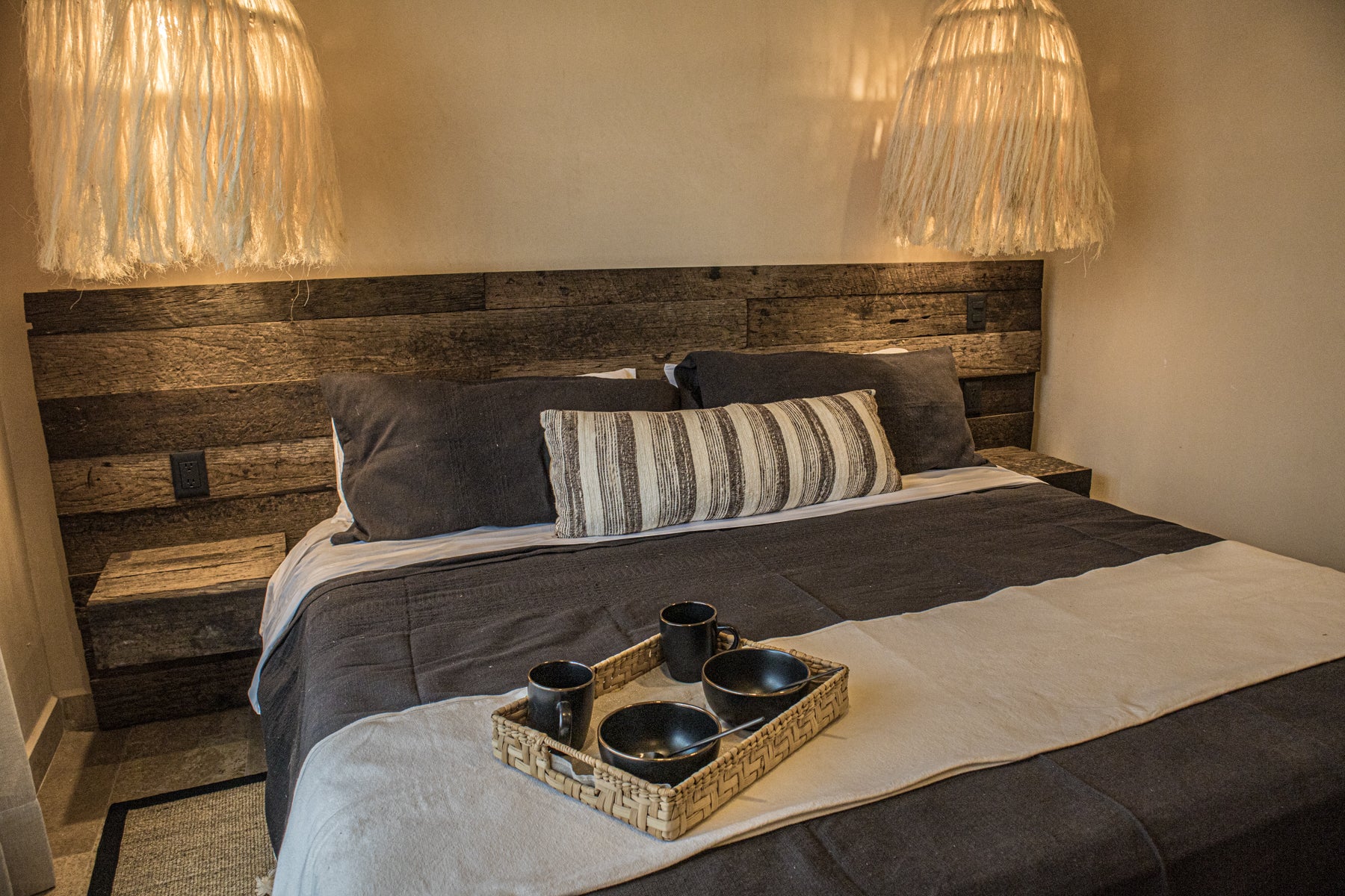 cama king size de madera con cojines decorativos, lámparas de techo tejidas con fibras naturales