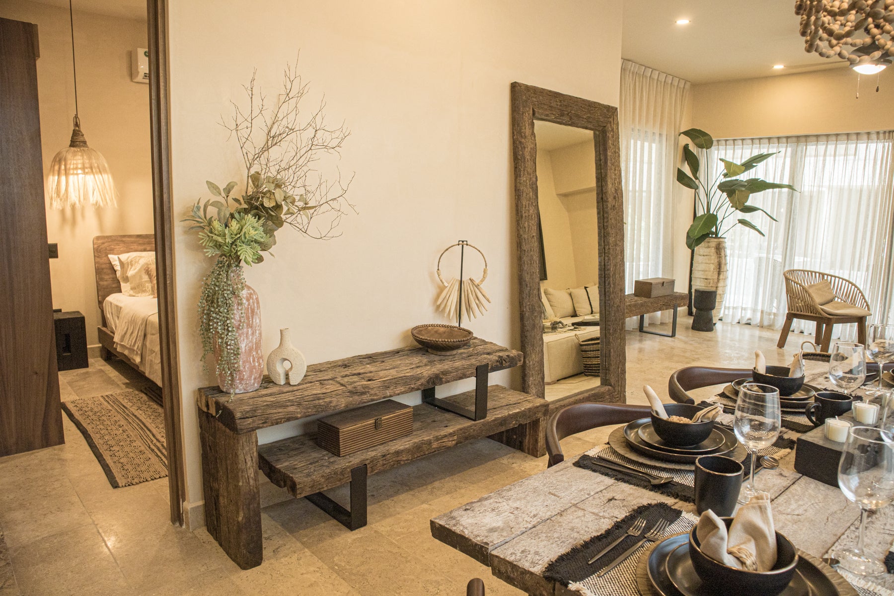 Espacio interior decorado con credenza vintage, vajilla negra, banco de madera, espejo de marco rústico y plantas naturales. Todo de Prisma muebles Tulum