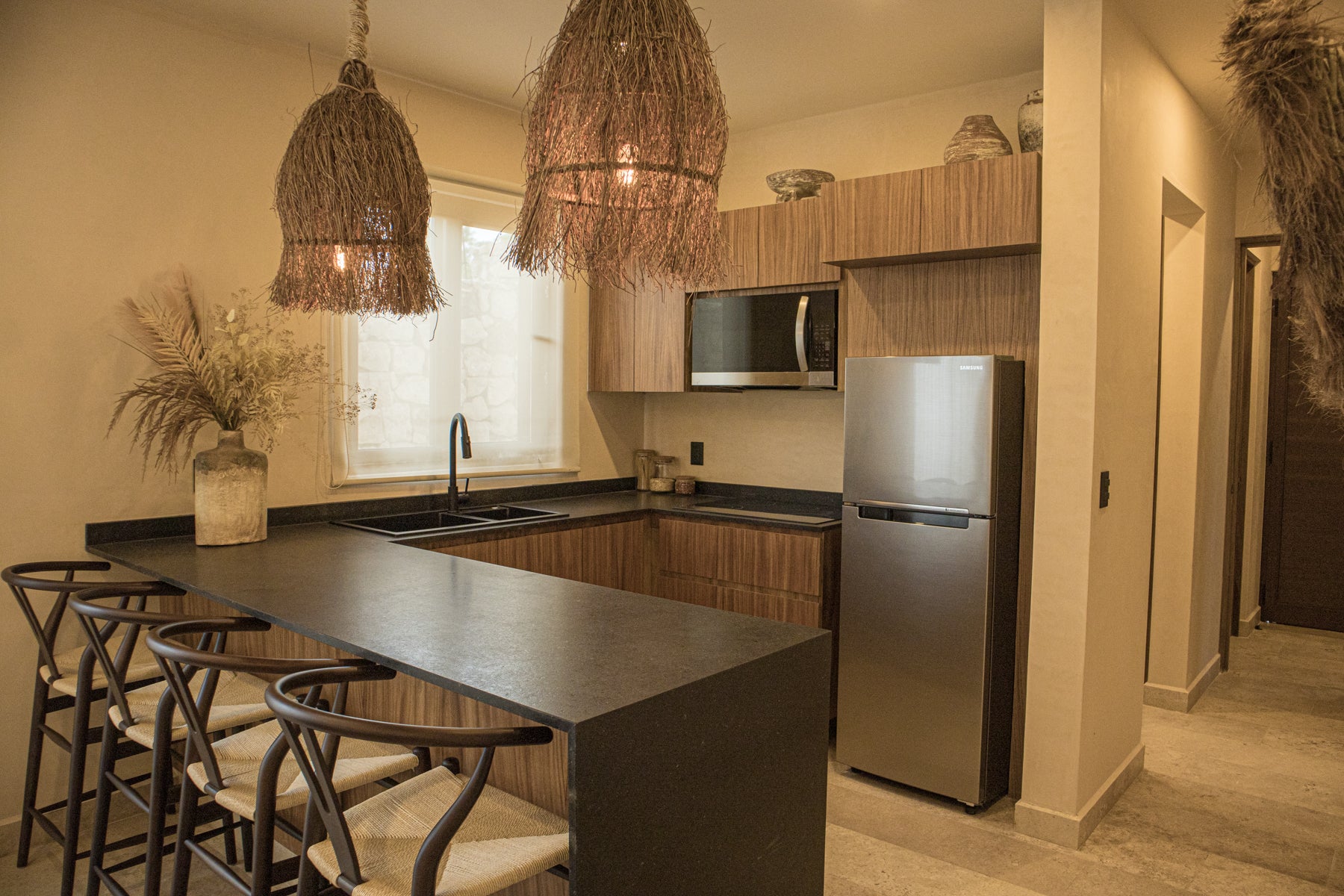 Cocina con diseño contemporáneo, barra desayunadora, sillas de madera tejidas y decoración rústica. Encuentra muebles para cocinas en Prisma Muebles Tulum.