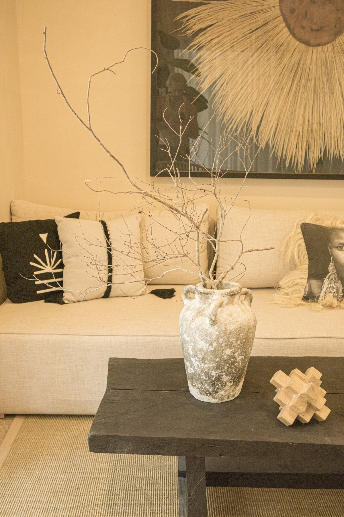 Sala decorada con sofá en tonos neutros, mesa de centro de madera oscura cojín con diseño étnico. Todo de Prisma Muebles Tulum