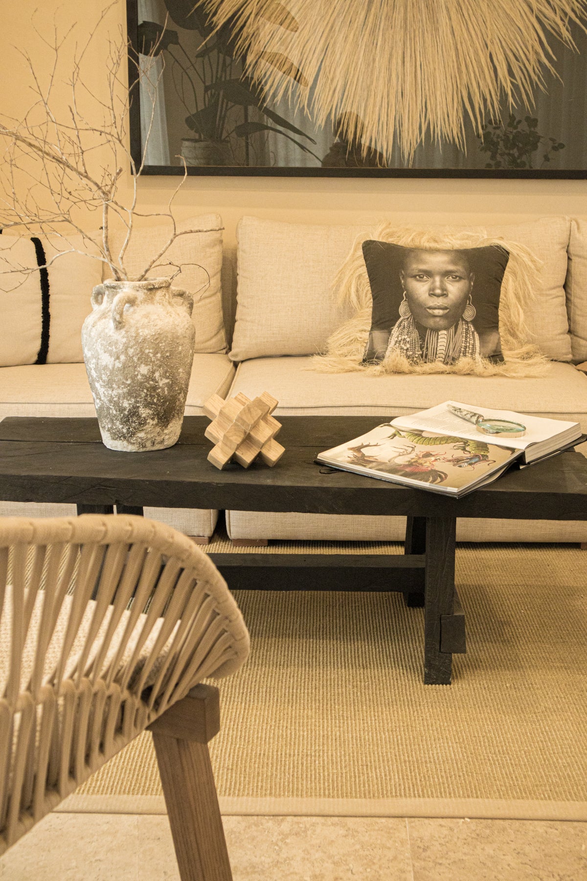 Sala decorada con sofá en tonos neutros, mesa de centro de madera oscura con detalles artesanales y cojín con diseño étnico. Todo de Prisma Muebles Tulum