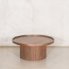 Mesa de centro redonda de madera tono nogal con base cilíndrica y borde elevado, ideal para salas modernas en climas tropicales | Prisma Muebles.