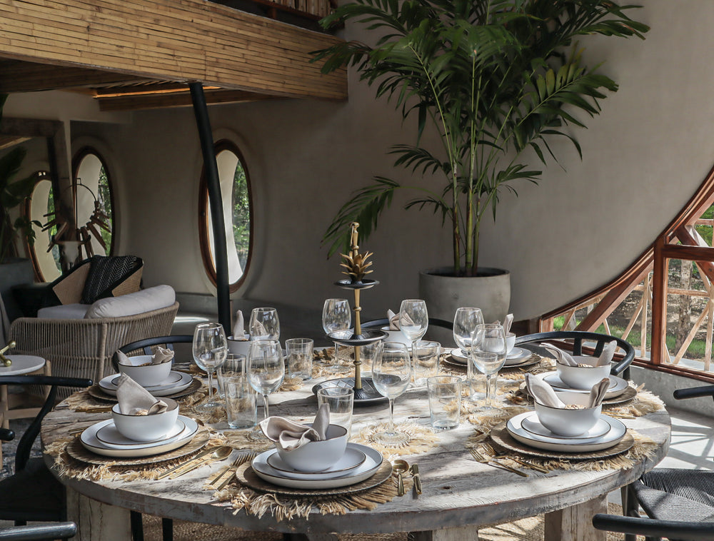 Mesa redonda de madera con vajilla elegante en comedor tropical, ideal para espacios modernos en Cancún, Playa del Carmen y Tulum.